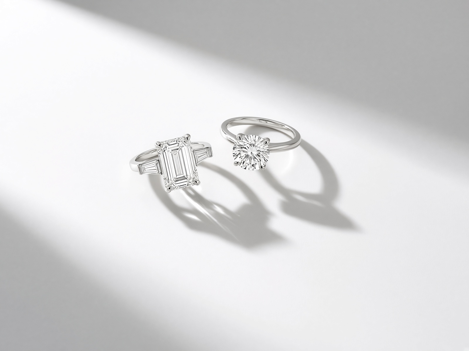 An emerald-cut ring and a round brilliant on a white studio sweep